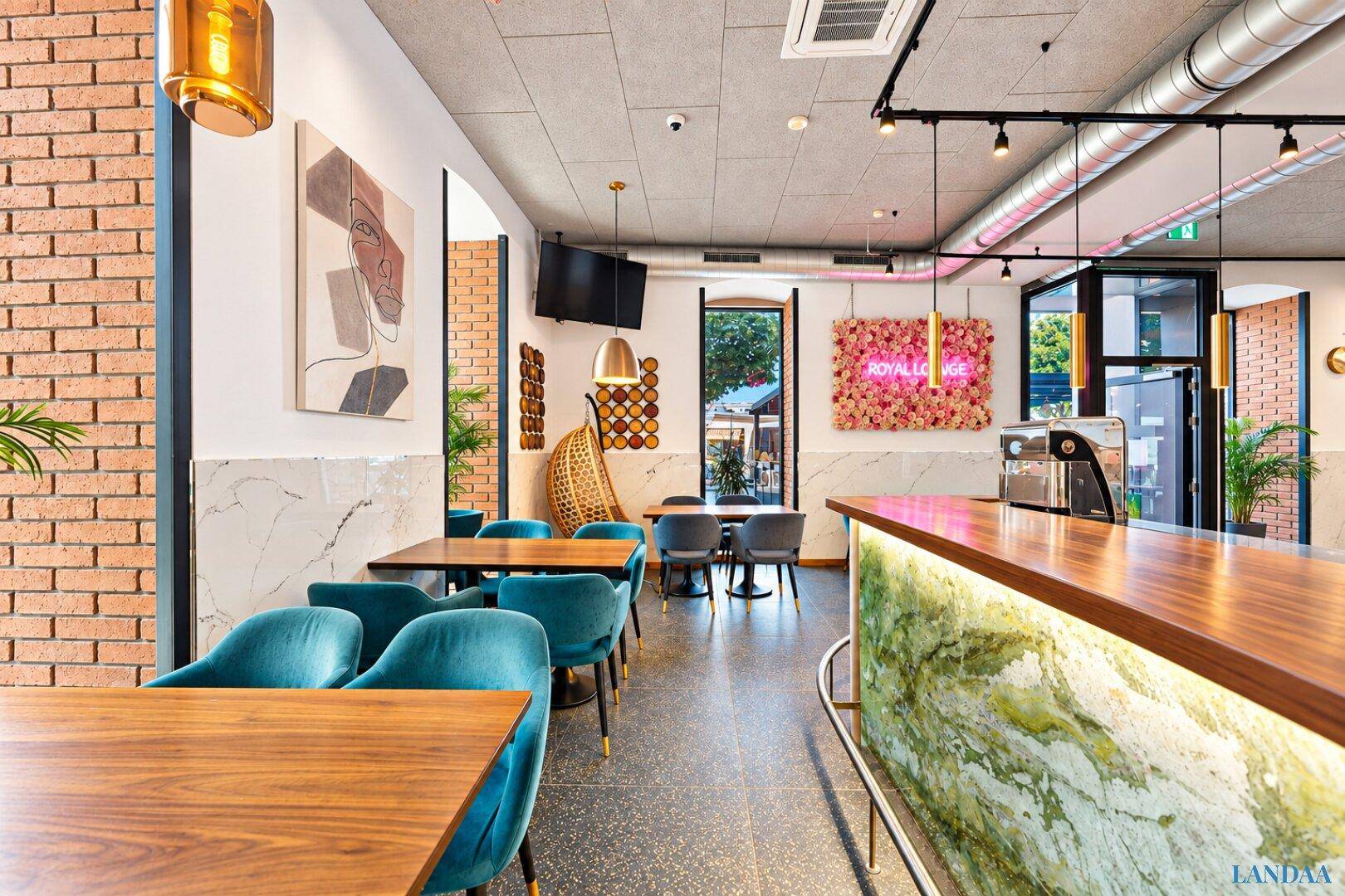 Heller Restaurantbereich mit Bar, Holztischen und großen Fenstern, die viel Tageslicht hereinlassen.
