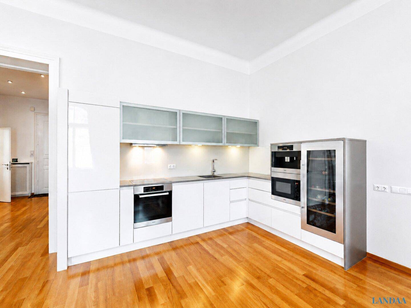 Moderne weiße Einbauküche mit glänzenden Fronten, integrierten Geräten und Holzboden.