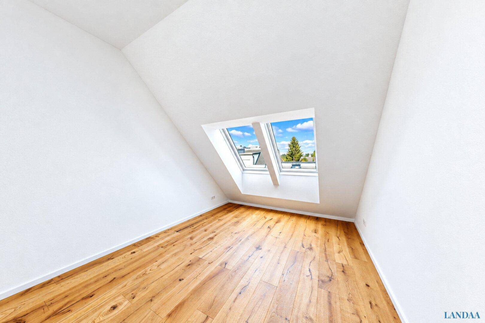 Helles, leeres Zimmer mit Holzboden, Dachschräge und einem großen Dachfenster.