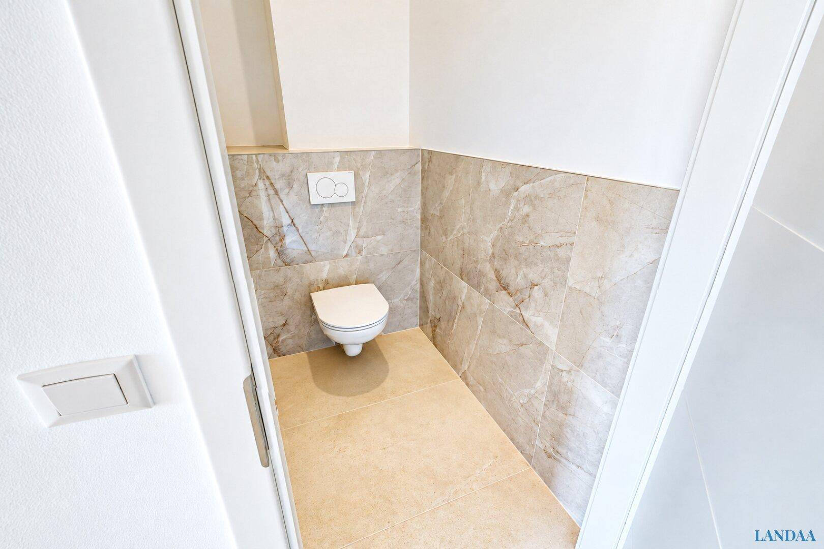 Separates Gäste-WC mit Wand-WC und eleganten Fliesen in Marmoroptik.