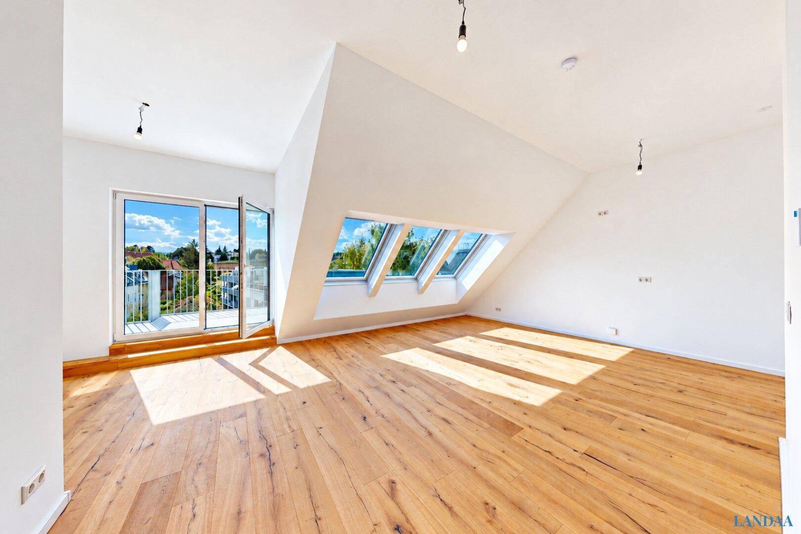 Helles Wohnzimmer mit Holzboden, Dachschrägen, Dachfenstern und Zugang zum Balkon.