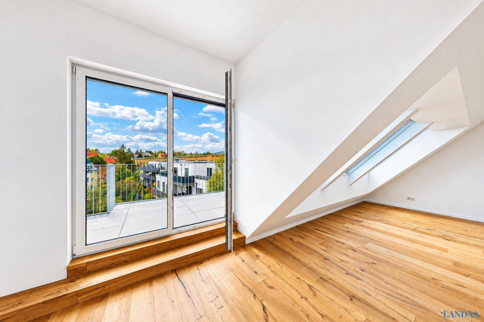 Lichtdurchflutetes Zimmer mit Holzboden und großem Schiebefenster zum Balkon.