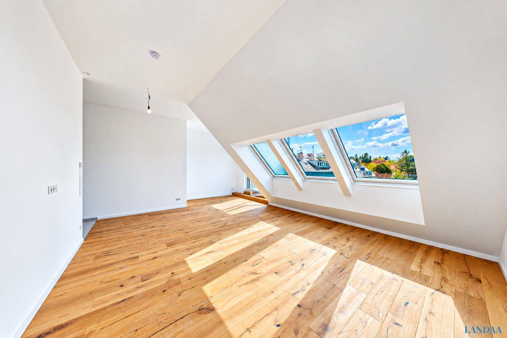 Geräumiges, leeres Wohnzimmer mit Holzboden, Dachschrägen und großen Dachfenstern.