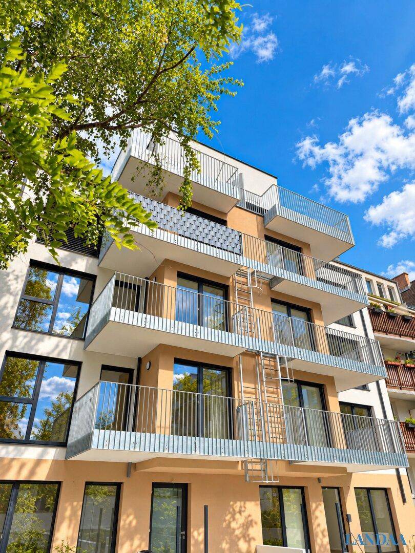 Moderne Wohnhausfassade mit mehreren Balkonen und großen Fenstern unter blauem Himmel.