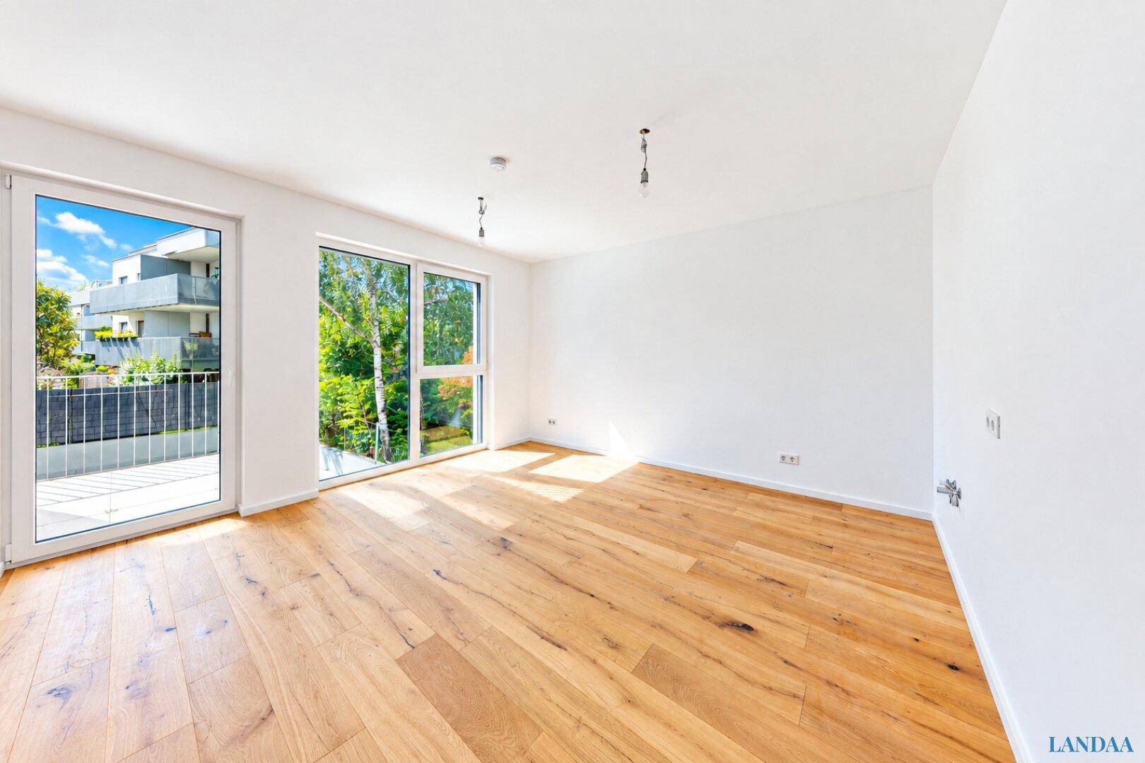 Heller, leerer Raum mit Holzboden und großen Fenstern, die viel Tageslicht hereinlassen.