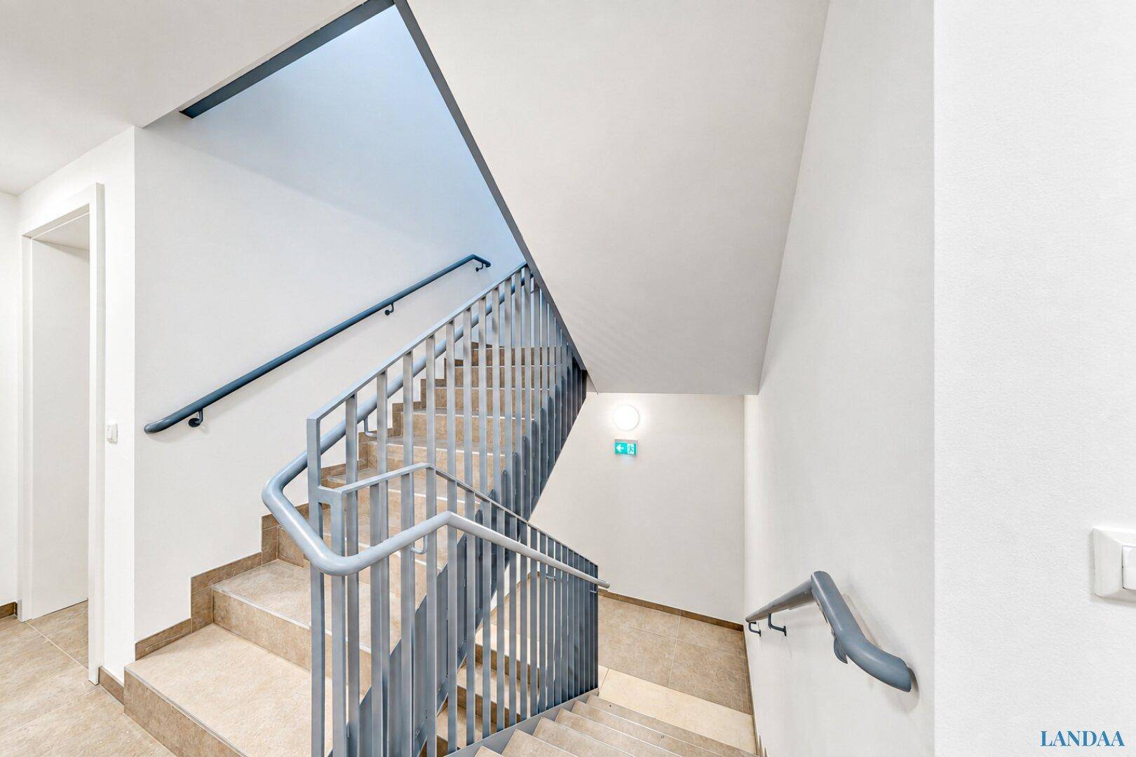 Modernes Treppenhaus mit Metallgeländer und gefliesten Stufen in einem Mehrfamilienhaus.