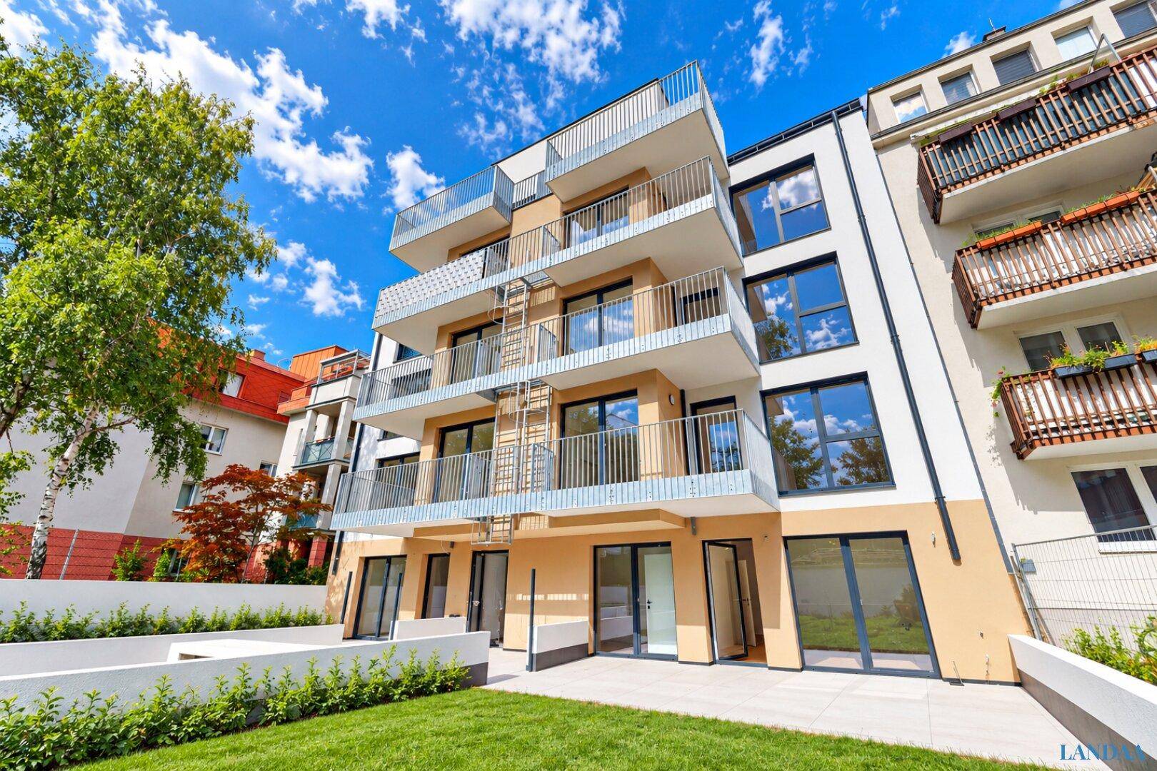 Moderne Wohnanlage mit mehreren Balkonen, großen Fenstern und einer gepflegten Rasenfläche.