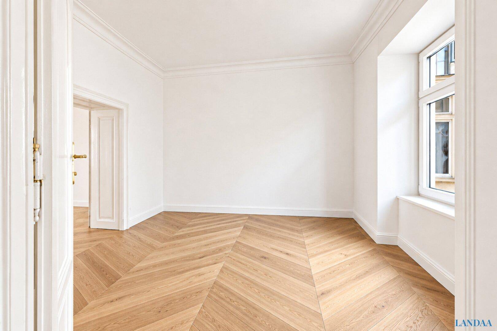 Ruhiges Zimmer mit hellem Fischgrätparkett und einem Fenster, das viel Licht hereinlässt.