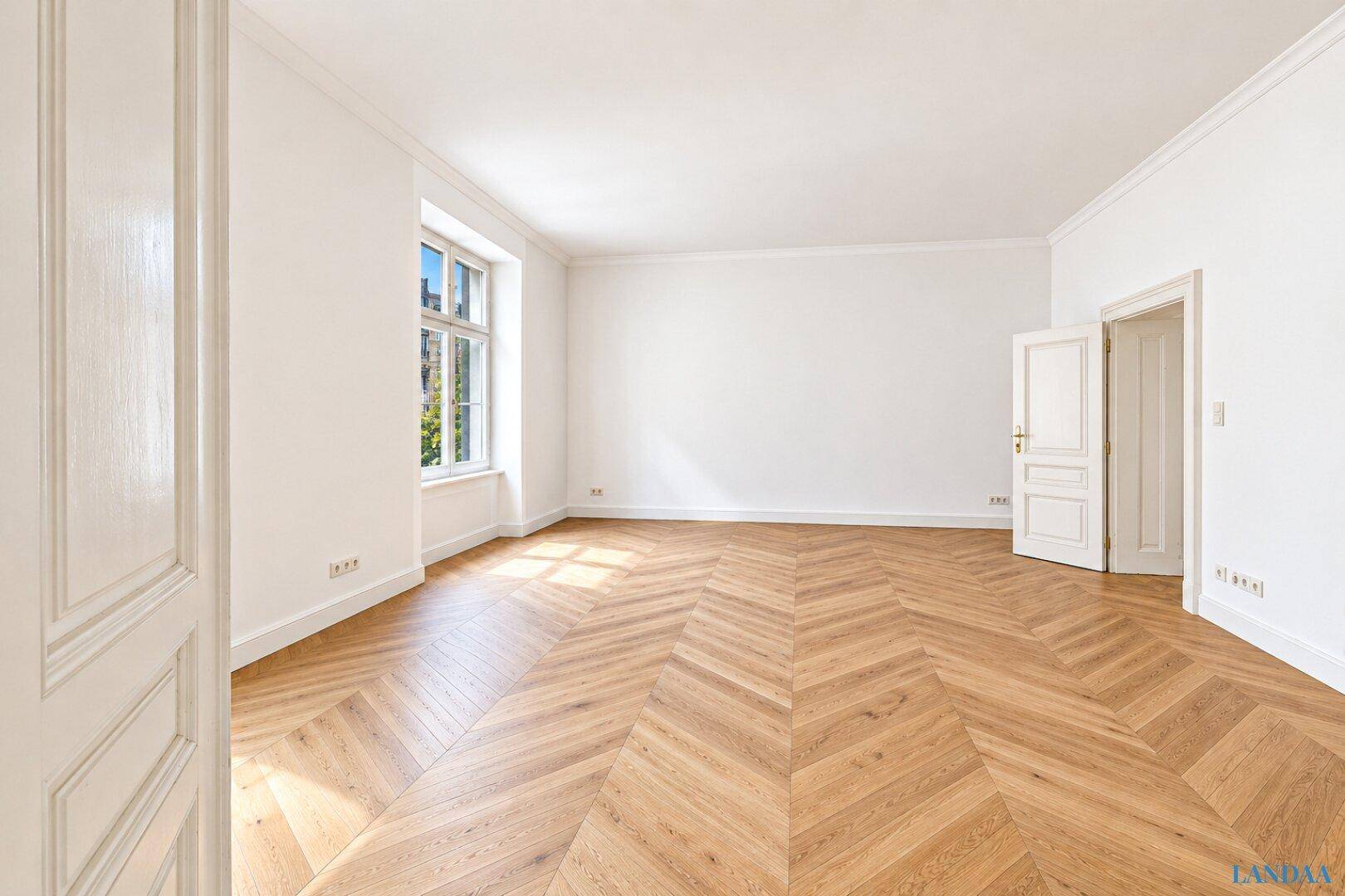 Geräumiges Zimmer mit klassischem Fischgrätparkett und einem Fenster, das viel Tageslicht spendet.