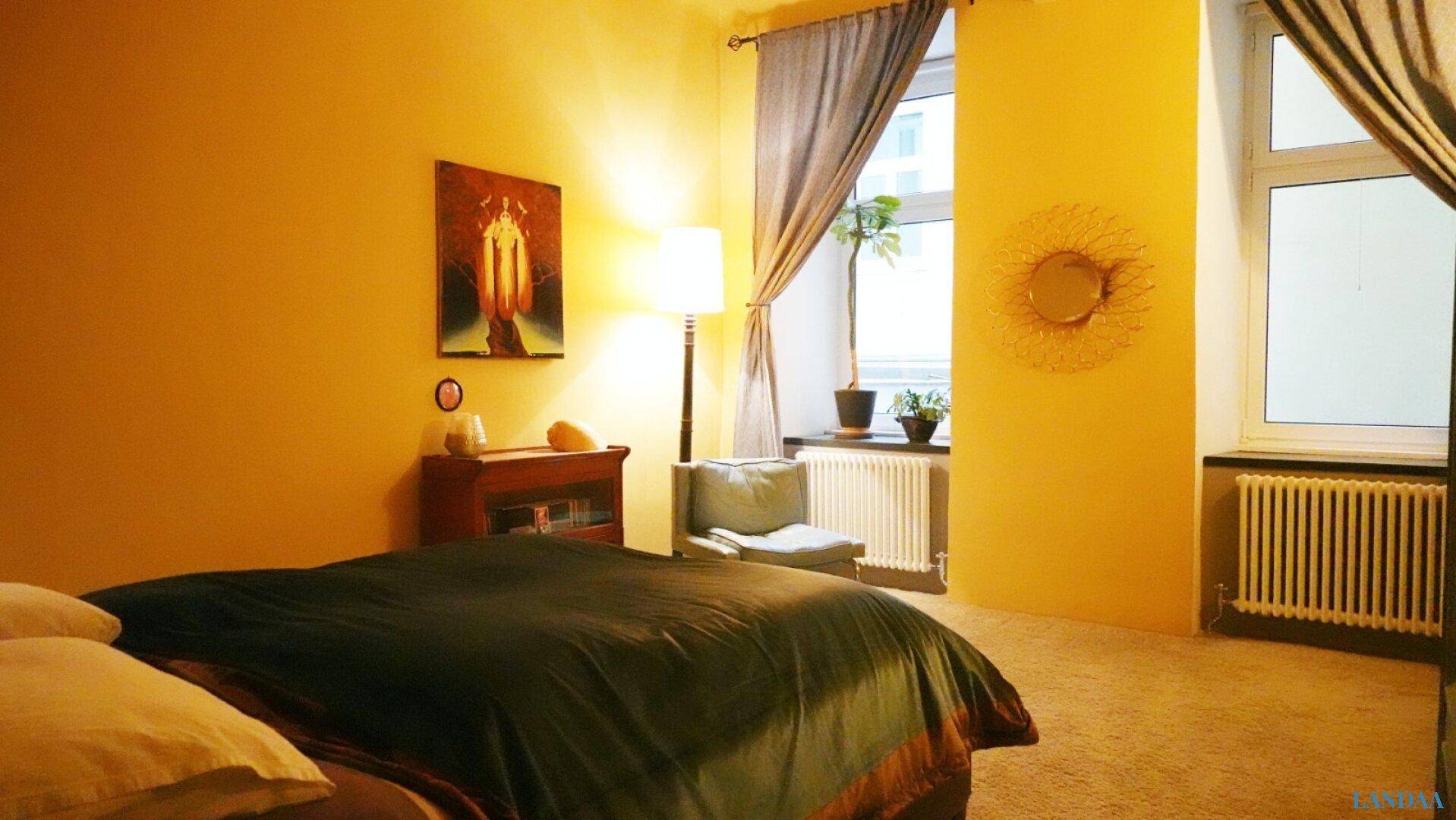 Helles Schlafzimmer mit gelben Wänden, großem Fenster und einem Heizkörper unter dem Fenster.