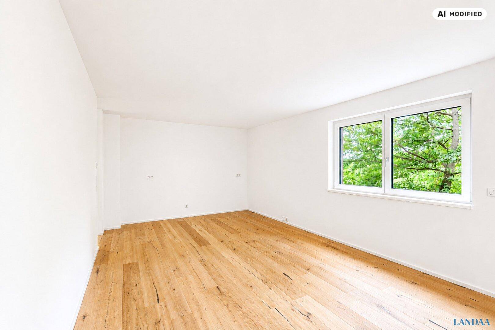 Heller, leerer Raum mit Holzboden und Fenster mit Blick ins Grüne.