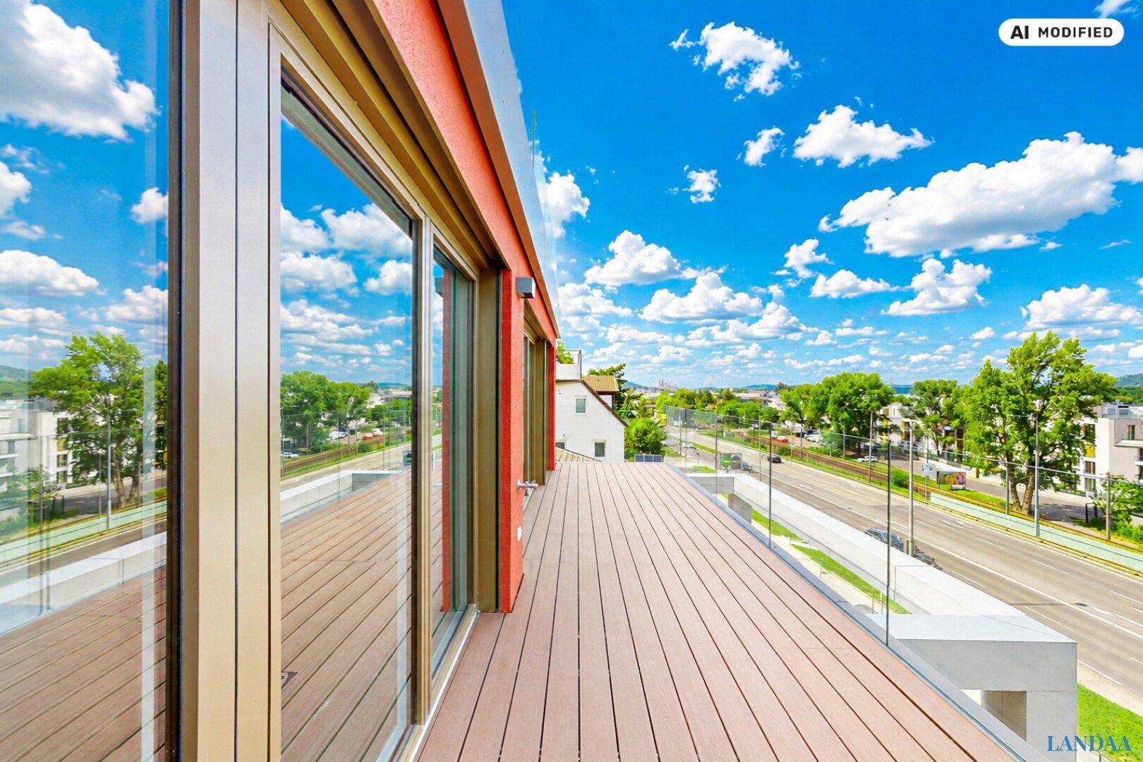 Weitläufige Terrasse mit Holzbelag und Glasgeländer, bietet einen weiten Blick auf die Umgebung und das Wasser.