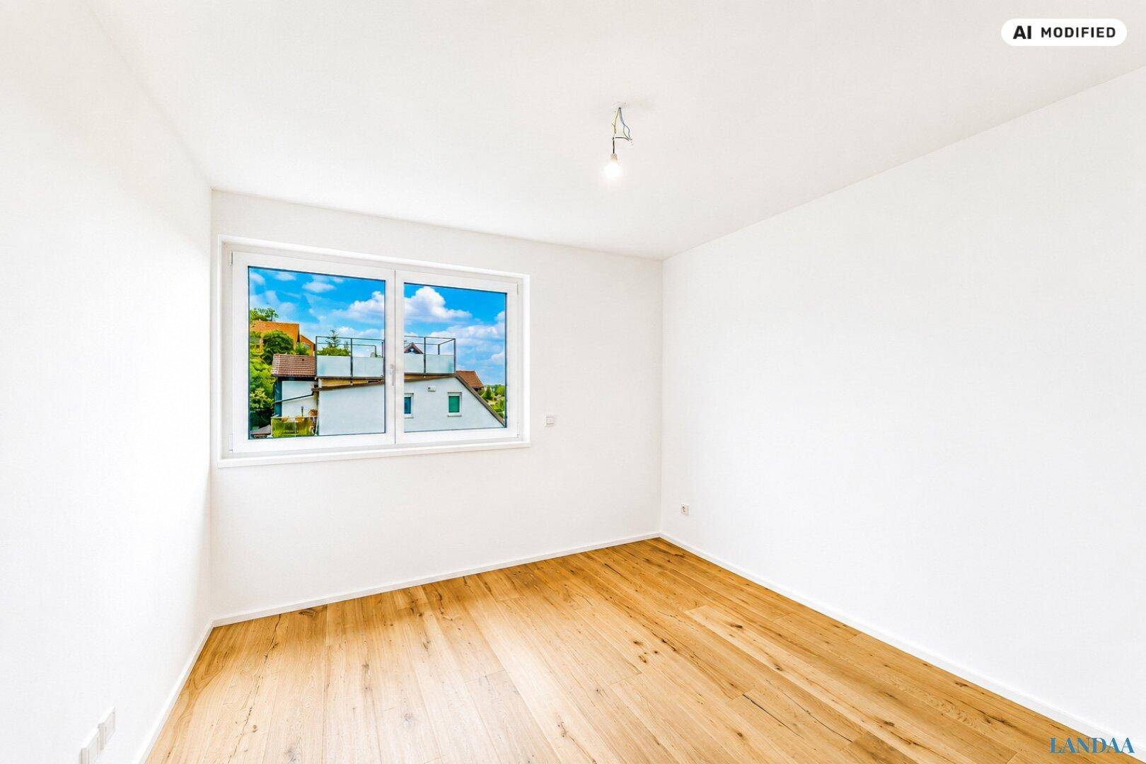 Heller, leerer Raum mit Holzboden und einem Fenster, das einen Blick auf die umliegenden Häuser bietet.