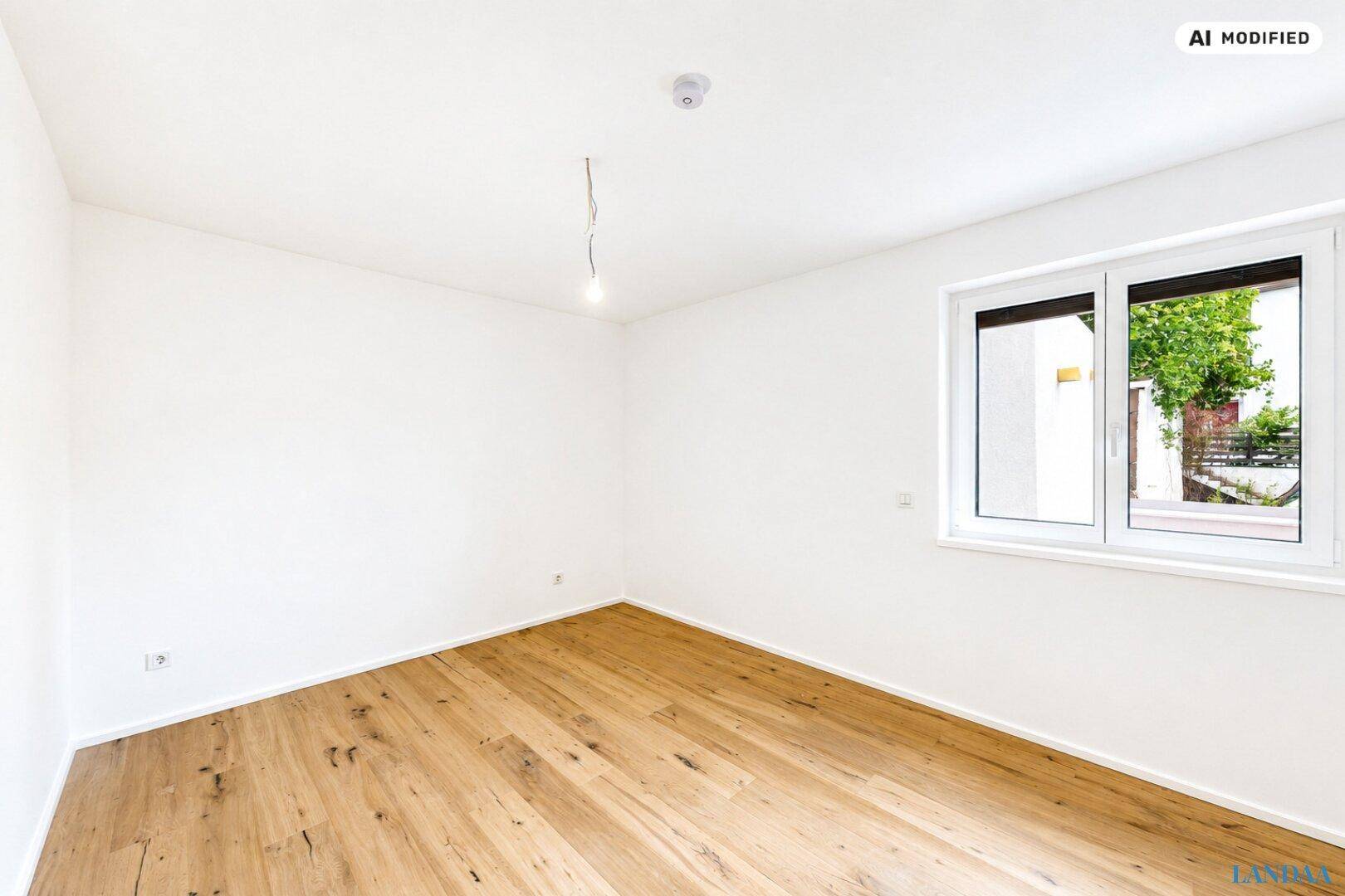 Leeres, helles Zimmer mit Holzboden und einem Fenster, das viel Tageslicht hereinlässt.