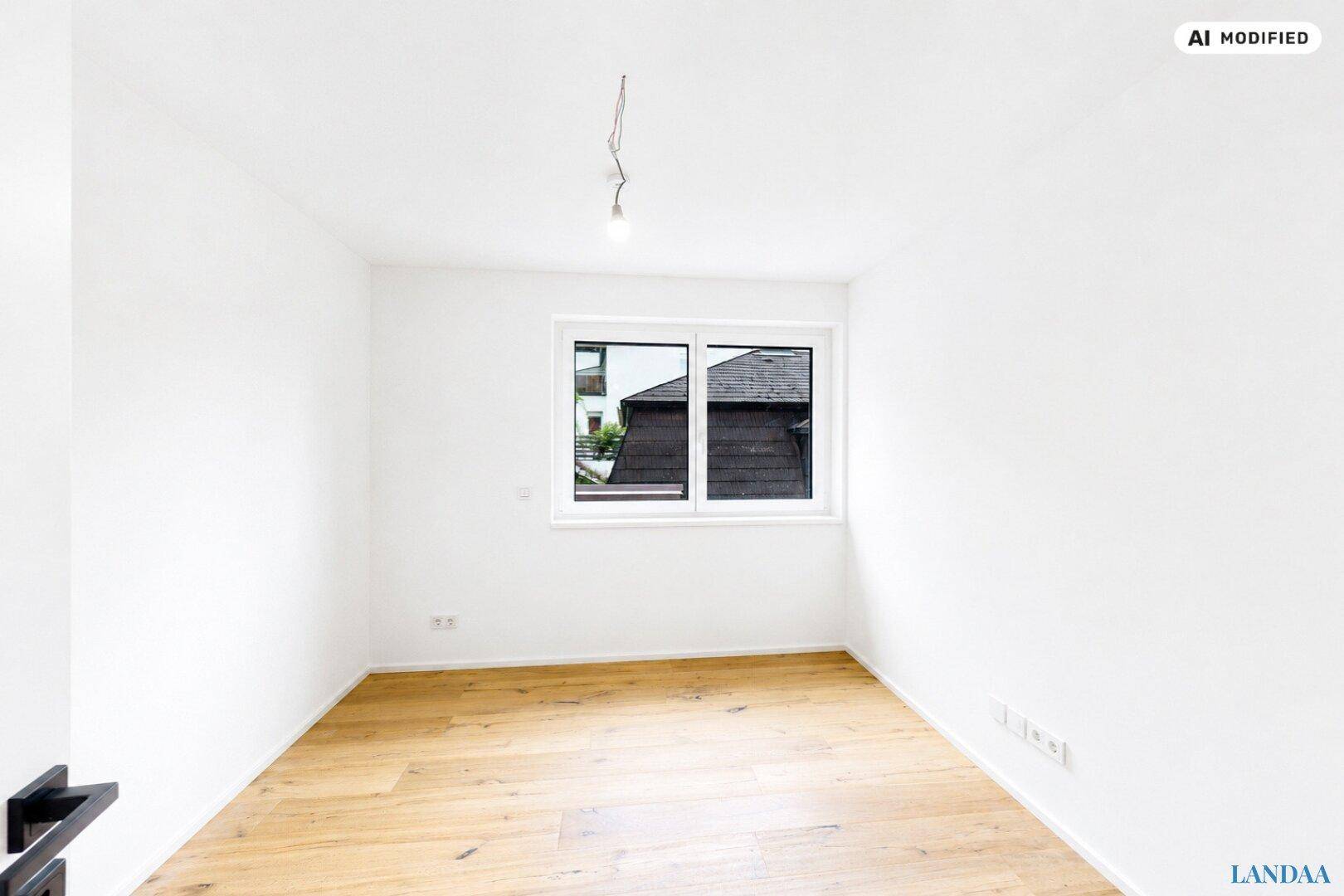 Helles, leeres Zimmer mit Holzboden und einem Fenster, das den Blick auf die Umgebung freigibt.