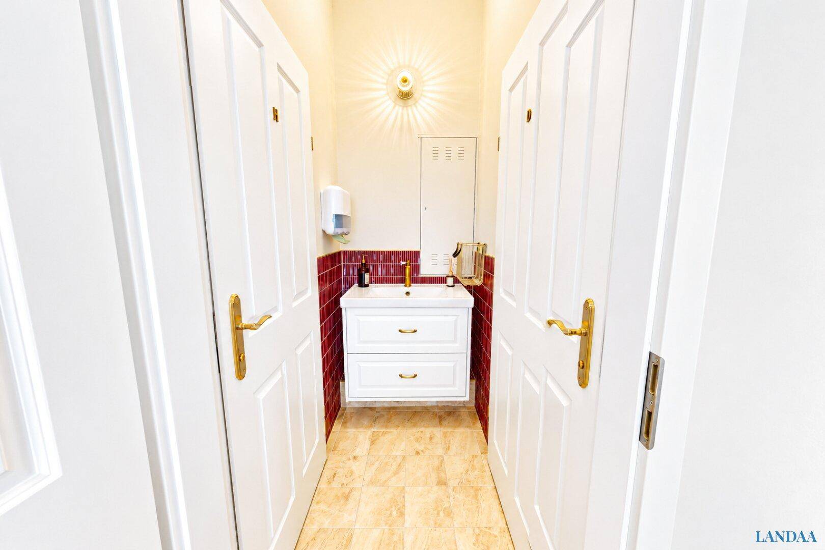 Heller Flur mit zwei Türen zu den Toiletten und einem Waschbeckenbereich dazwischen.