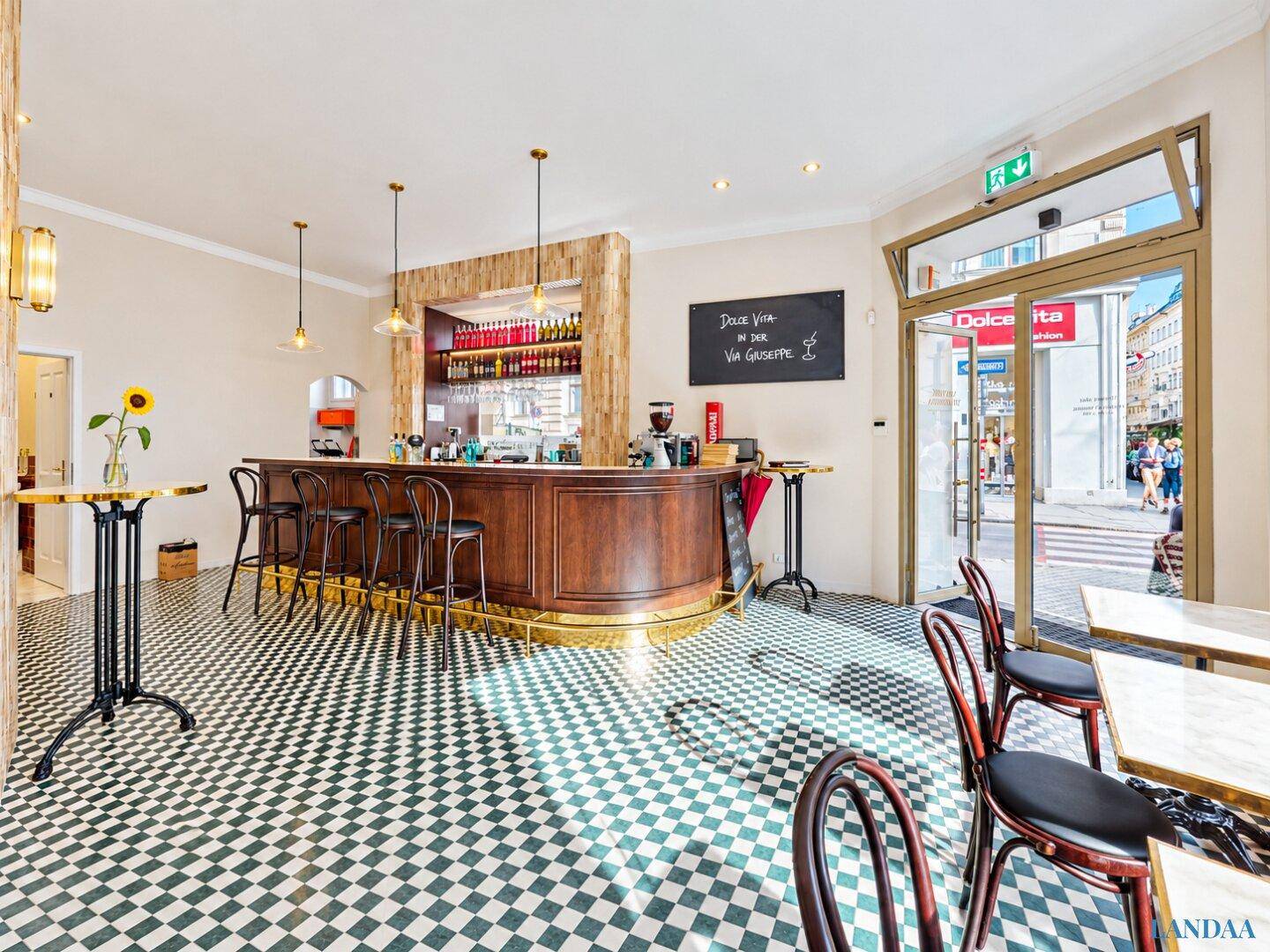 Einladender Eingangsbereich des Cafés mit Bar, Tischen und Blick auf die belebte Straße.