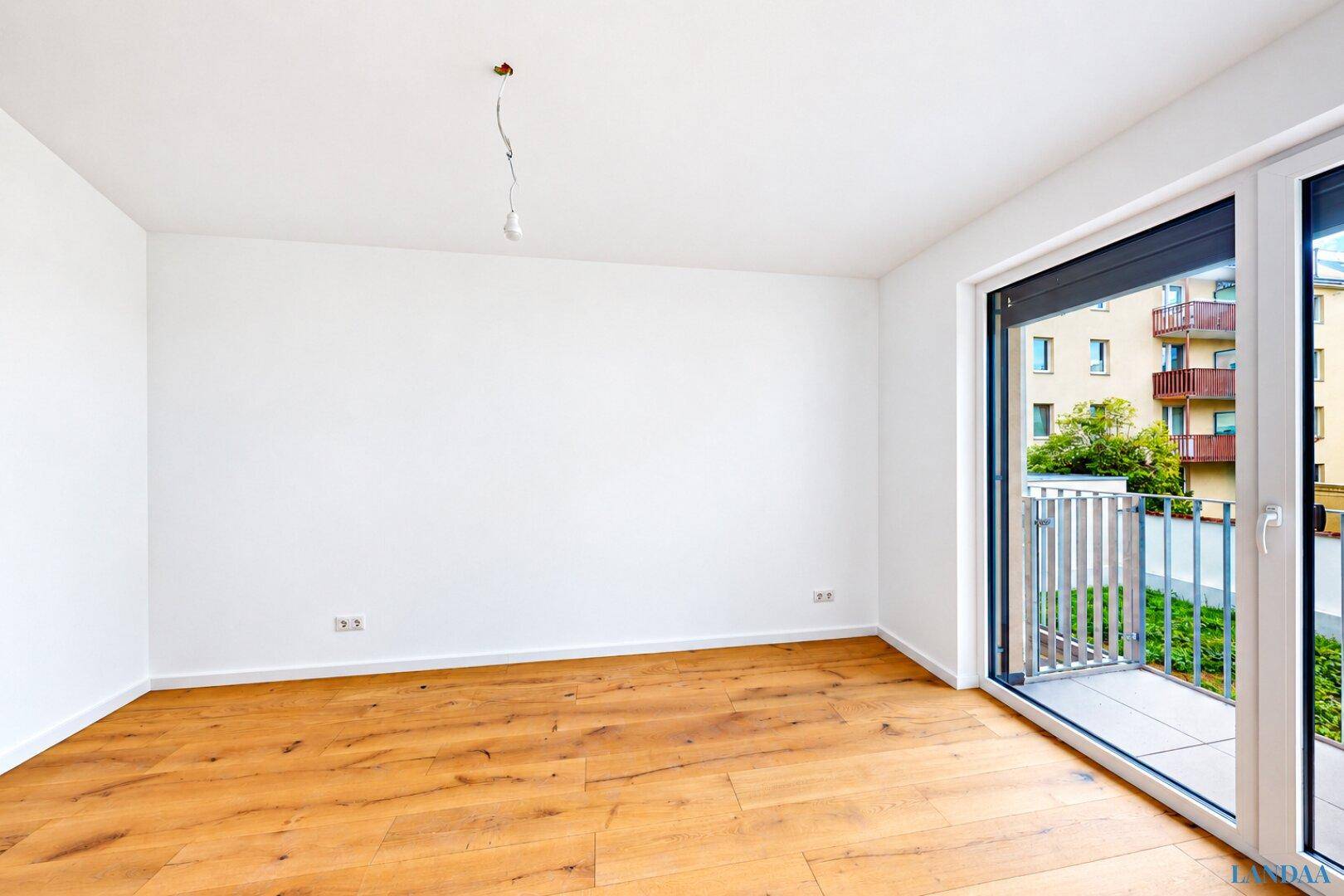 Unmöbliertes Zimmer mit Holzboden und Balkonzugang.