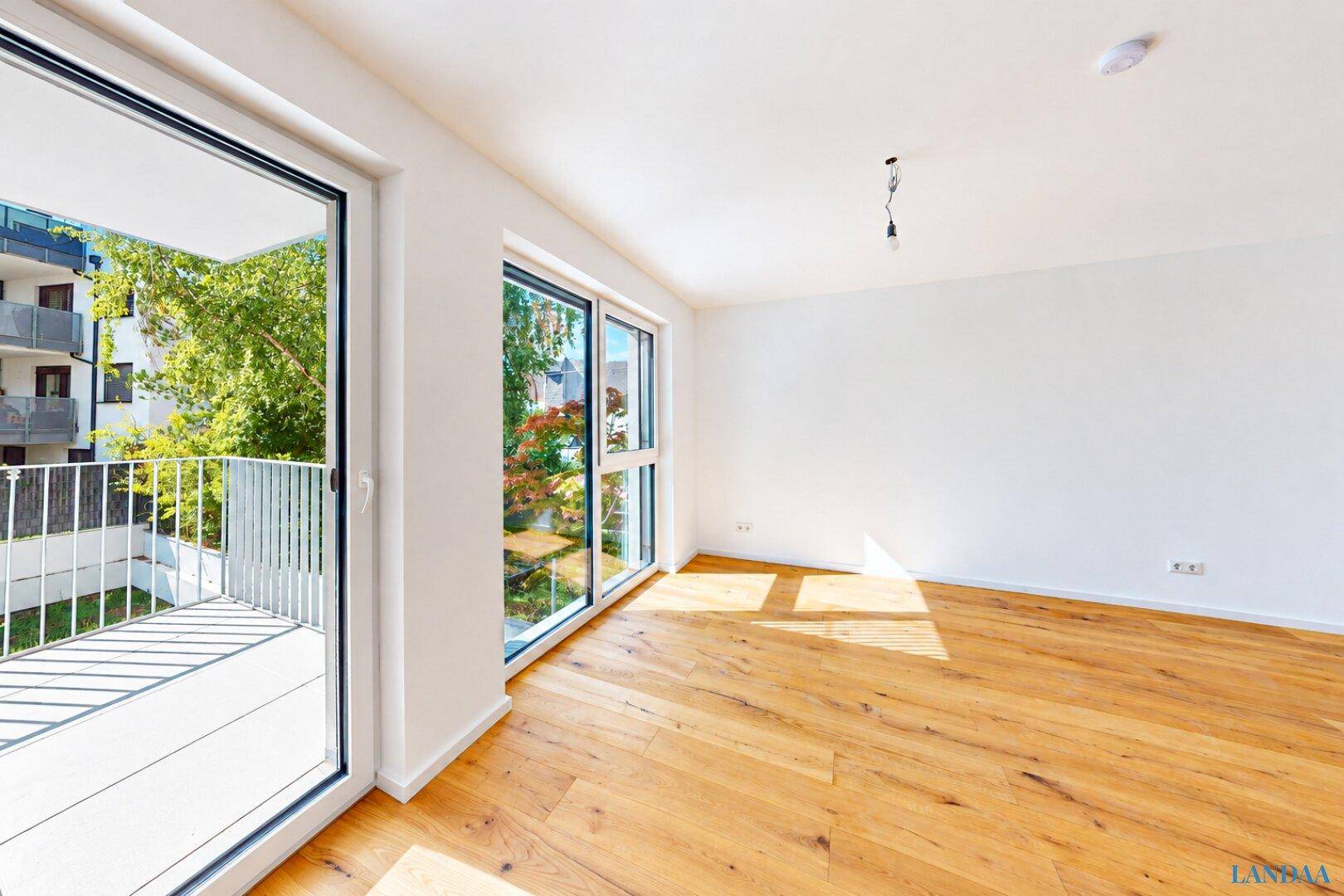 Helles Zimmer mit Holzboden und Zugang zu einem Balkon.