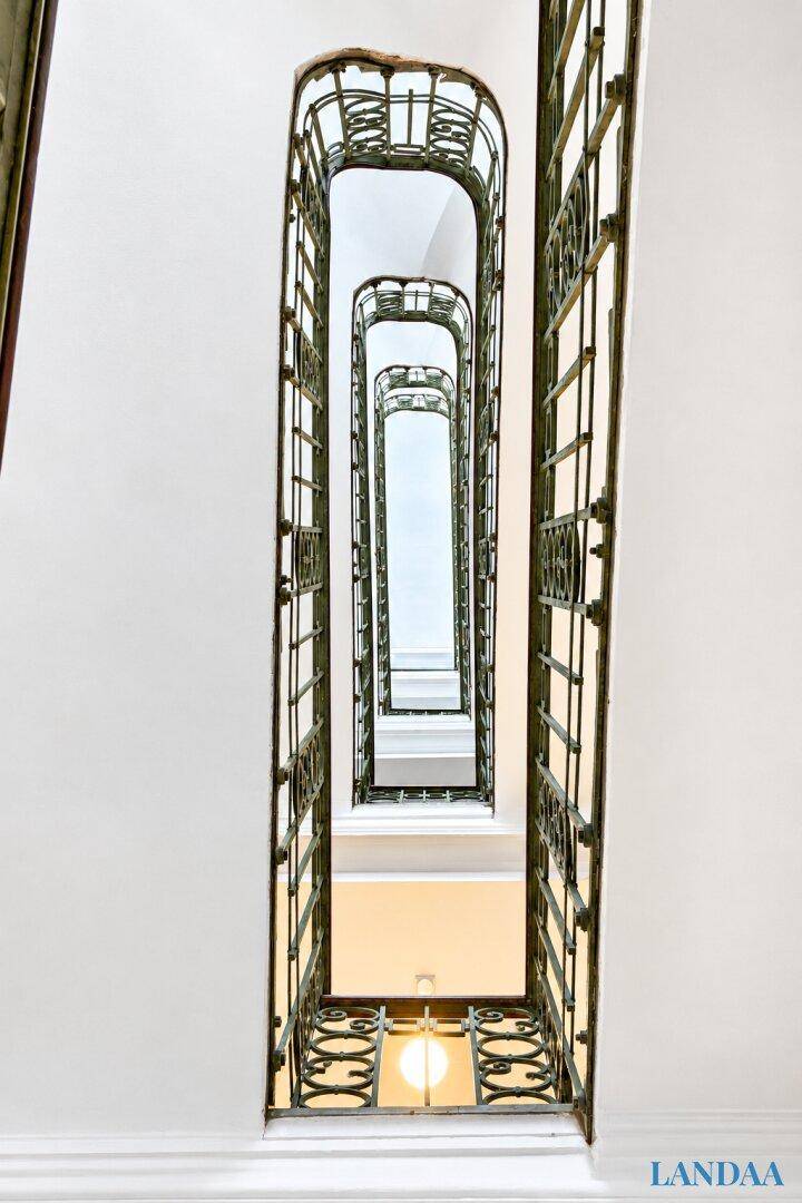 Historisches Treppenhaus mit kunstvollen Metallgeländern und hohen Decken, das die Stockwerke verbindet.