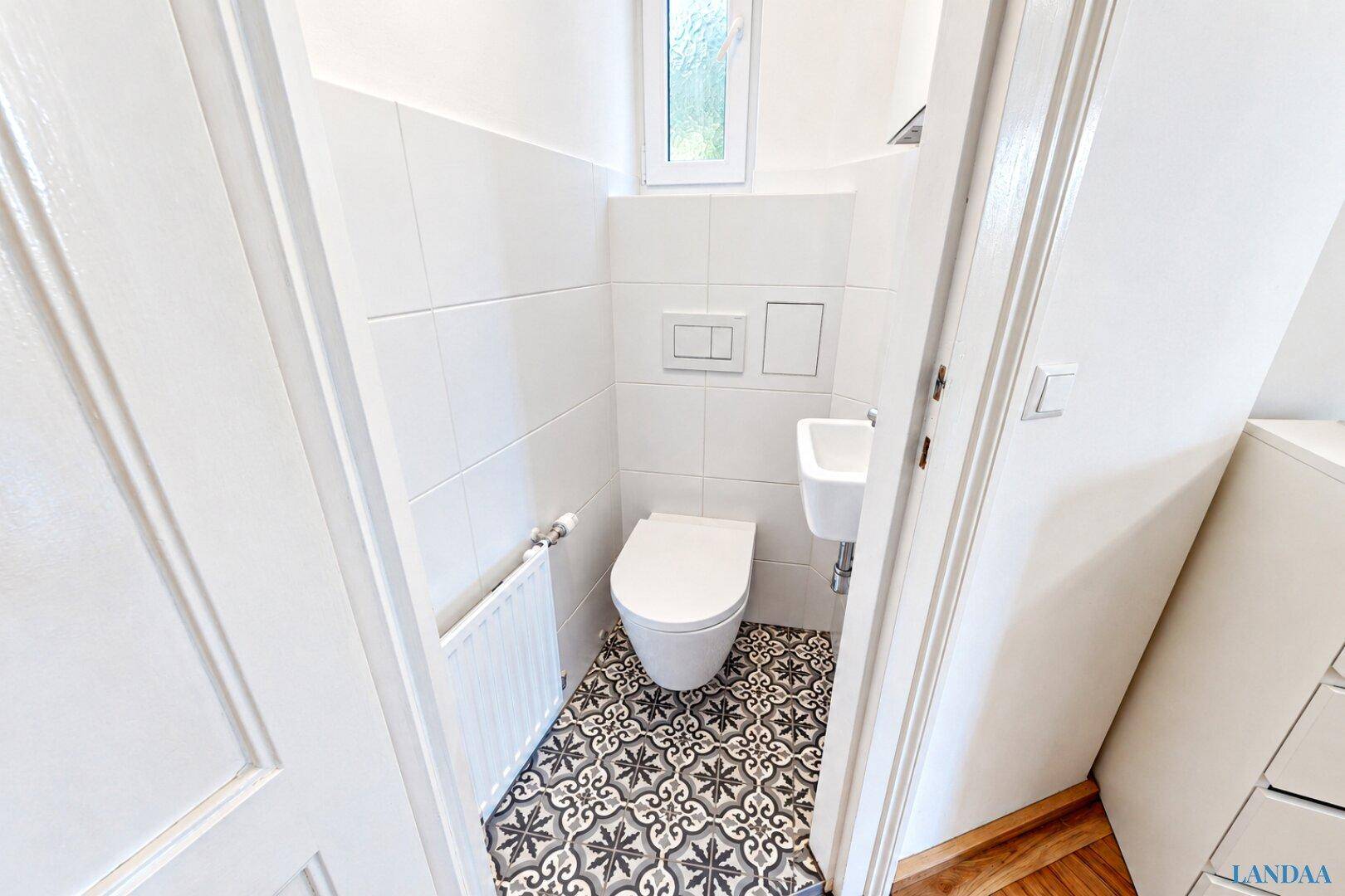 Kleines Gäste-WC mit modernem Wand-WC, Waschbecken und einem Fenster für natürliche Belüftung.
