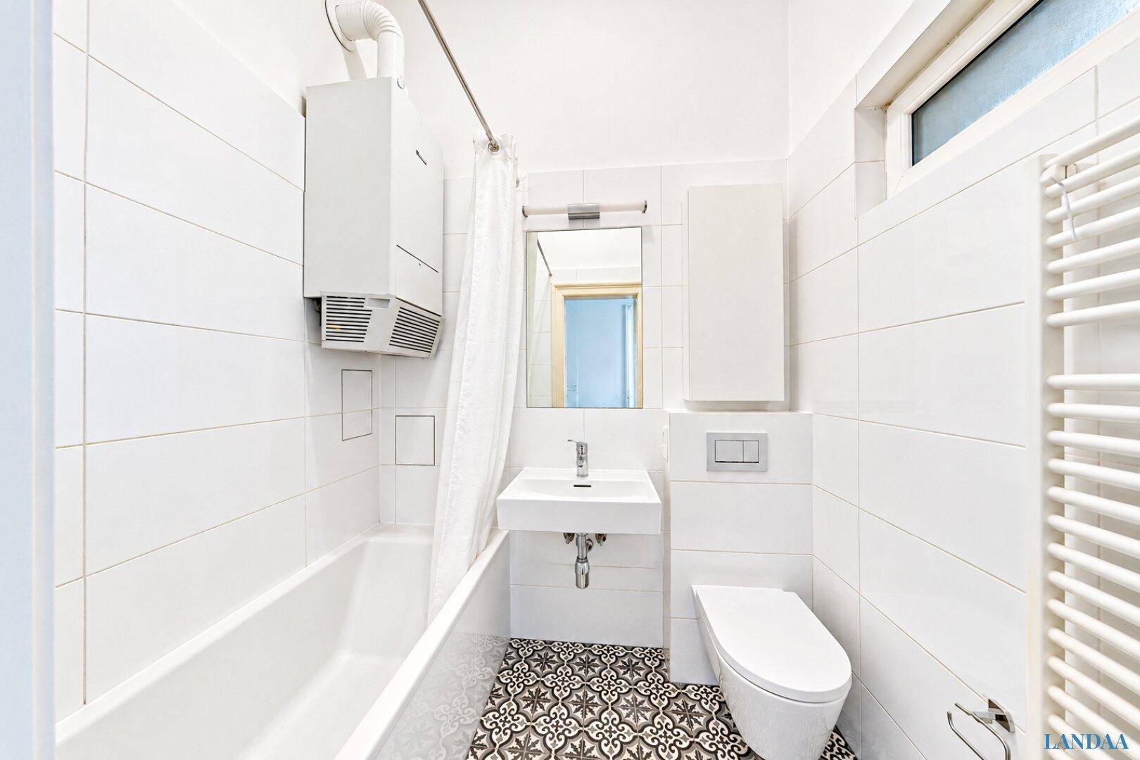Helles Badezimmer mit Badewanne, WC, Waschbecken und einem Fenster, ausgestattet mit weißen Fliesen.