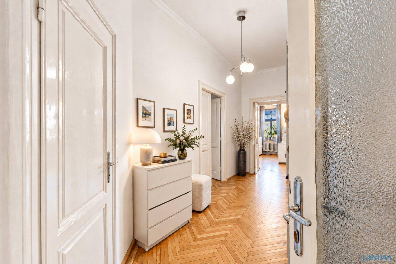 Heller Flur mit elegantem Fischgrätparkett, weißen Türen und einer modernen Kommode.