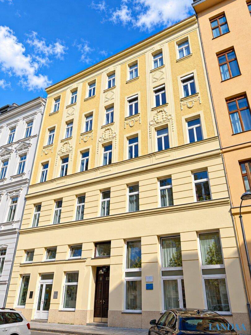 Ansicht der gelben Gebäudefassade mit mehreren Stockwerken und Fenstern, eingebettet in die Stadtlandschaft.
