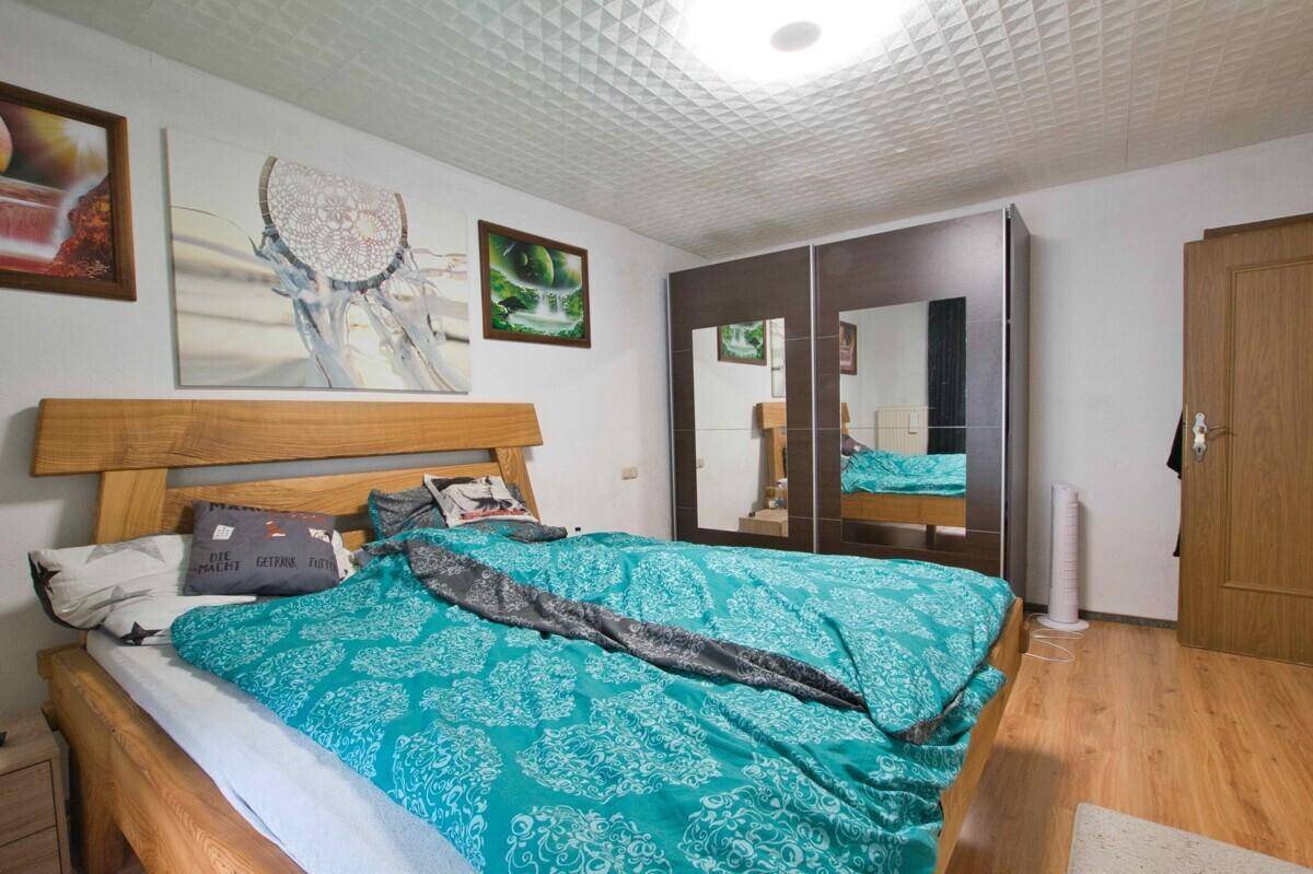 Schlafzimmer mit Doppelbett, großem Spiegelschrank und Laminatboden.