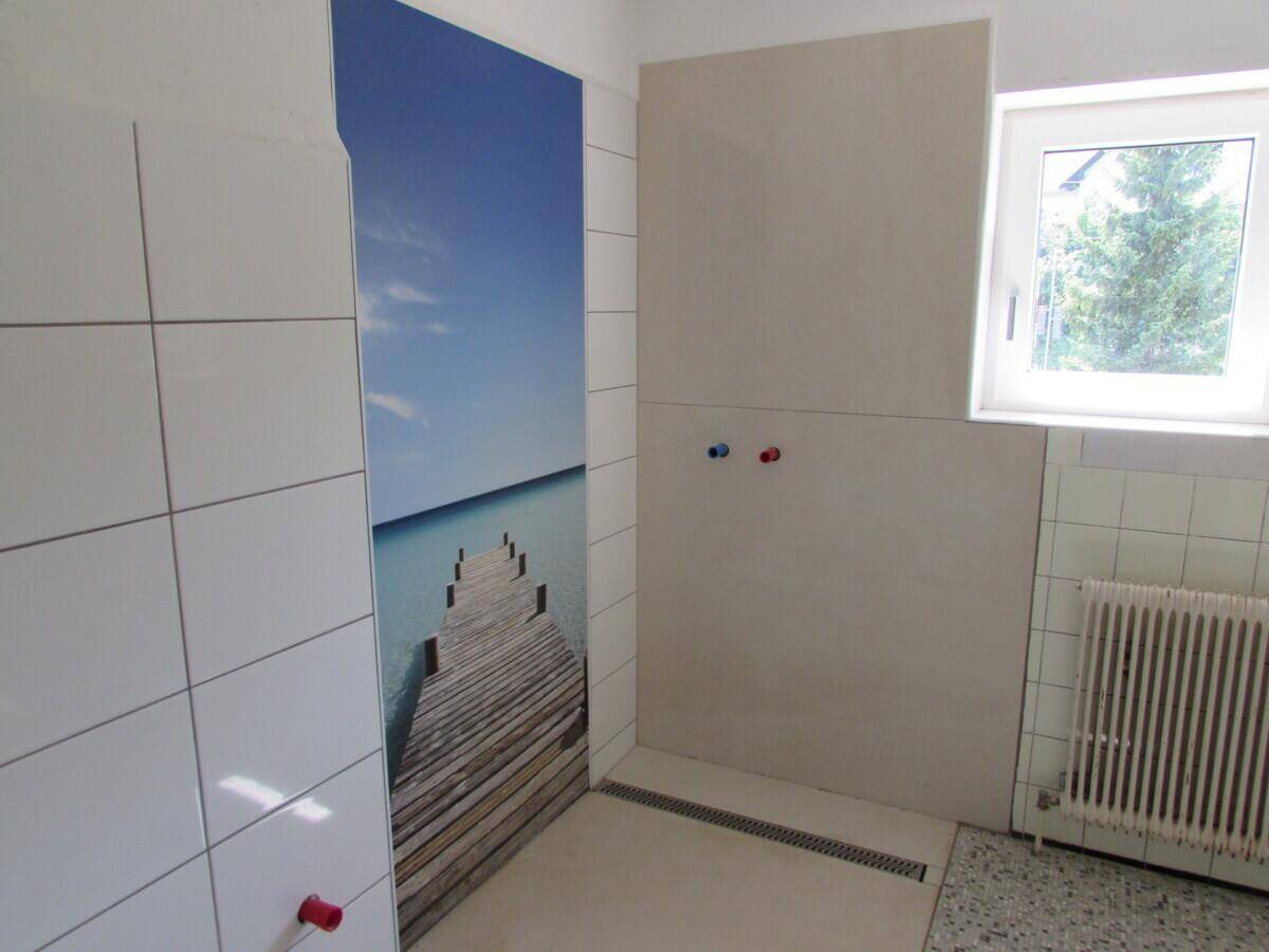 Badezimmer im Umbau mit weißen Fliesen, ebenerdiger Dusche und Fenster.