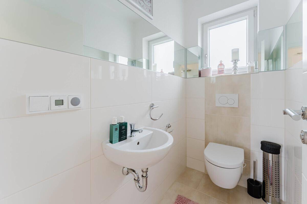 Gäste-WC mit wandhängendem WC, kleinem Waschbecken und hellen Fliesen.