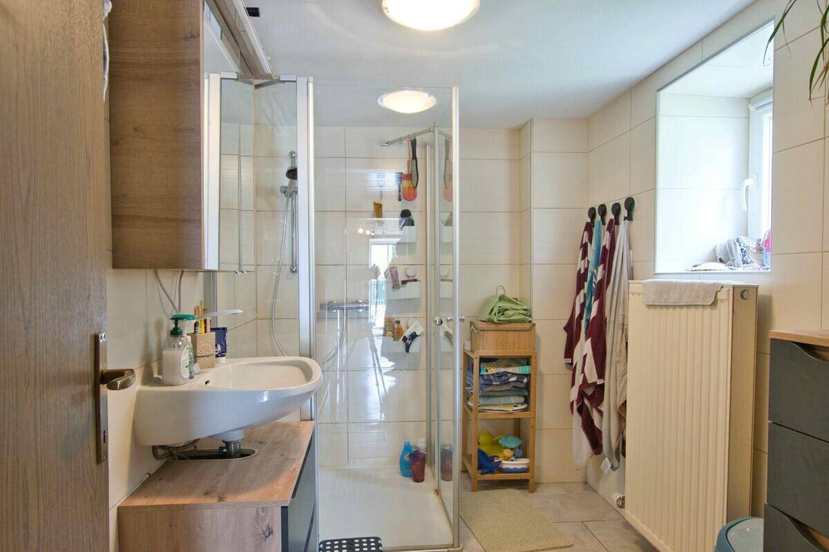Helles Badezimmer mit Duschkabine, Waschbecken und Fenster für Tageslicht.