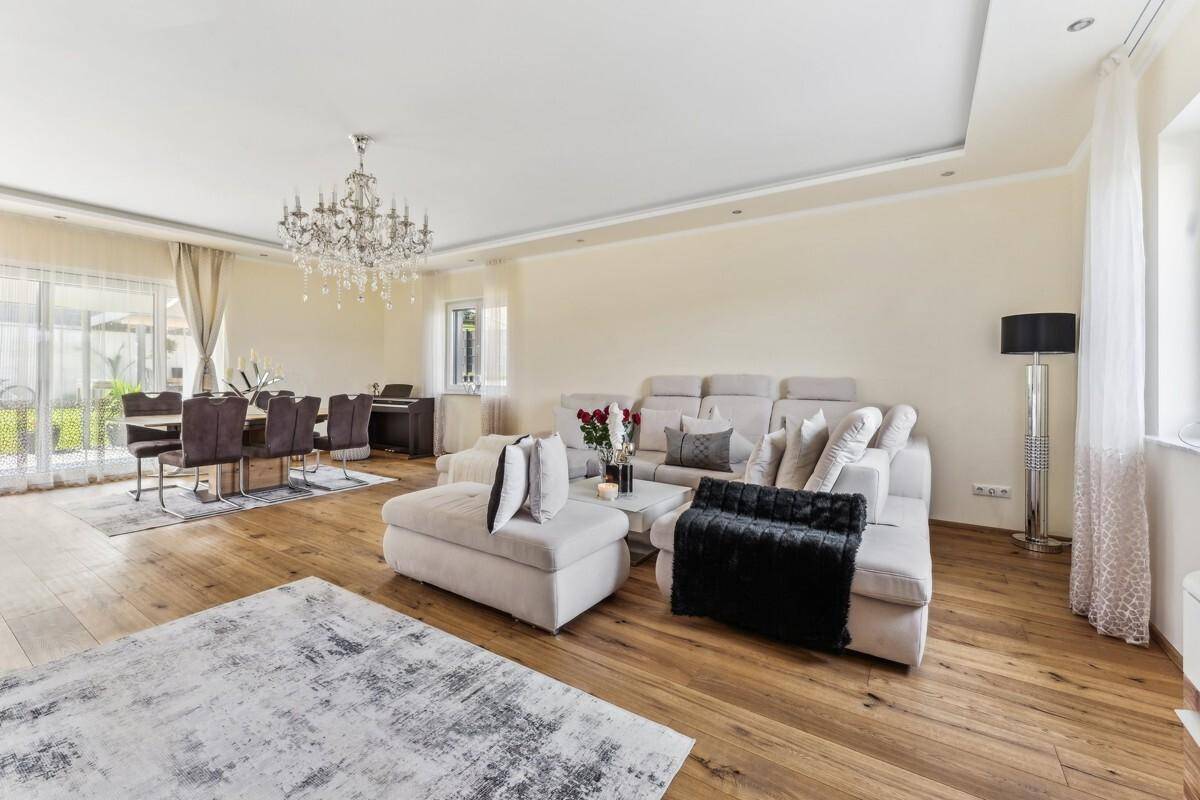 Geräumiger Wohn-Essbereich mit hellem Parkettboden, großem Sofa und elegantem Kronleuchter.