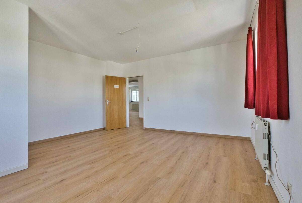 Helles Schlafzimmer mit Laminatboden, weißen Wänden und einer Holztür, ideal für ein gemütliches Zuhause.