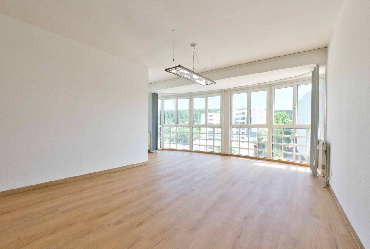 Heller, leerer Wohnraum mit großen Fenstern, die viel Tageslicht hereinlassen und einen weiten Blick bieten.