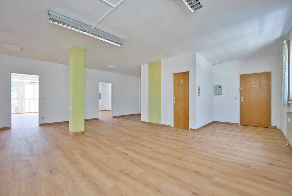 Geräumiger Bürobereich mit Laminatboden, weißen Wänden und mehreren Türen, teilweise mit grünem Akzent.