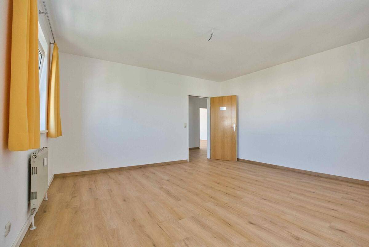 Leeres Schlafzimmer mit Laminatboden, weißen Wänden und einer Holztür, bereit zur individuellen Gestaltung.