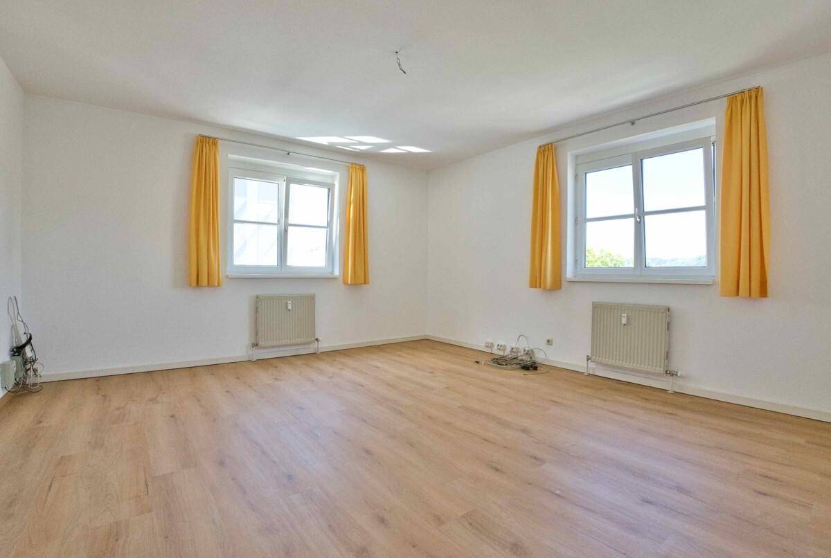 Helles Schlafzimmer mit zwei Fenstern, gelben Vorhängen und einem warmen Laminatboden.