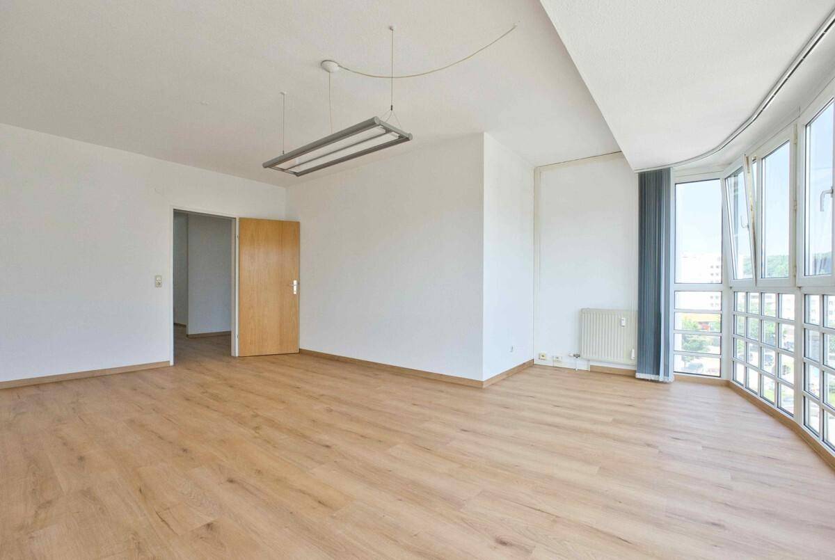 Geräumiger Wohnbereich mit geschwungener Fensterfront, hellem Laminatboden und viel natürlichem Licht.