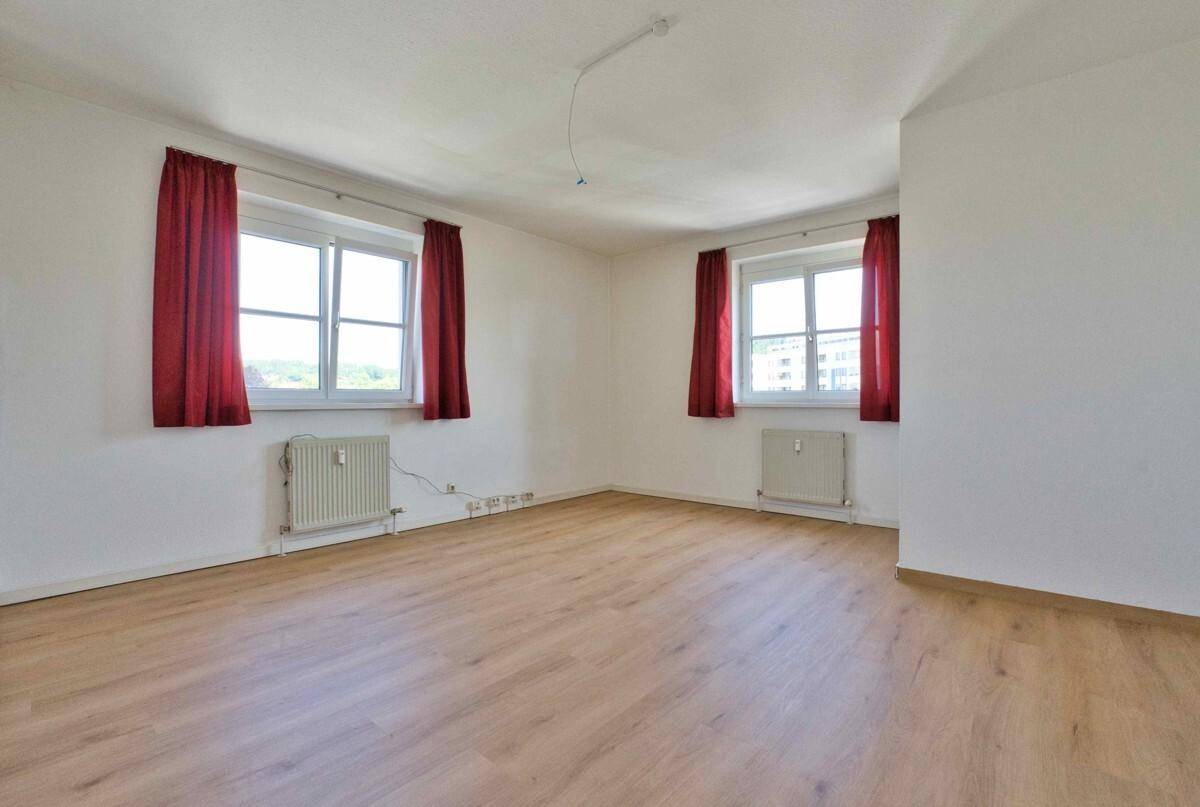 Geräumiges Schlafzimmer mit Laminatboden, weißen Wänden und zwei Fenstern mit roten Vorhängen.