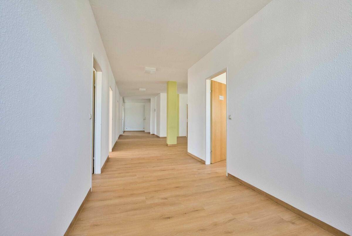 Langer, heller Flur mit Laminatboden und mehreren Türen, der verschiedene Räume miteinander verbindet.