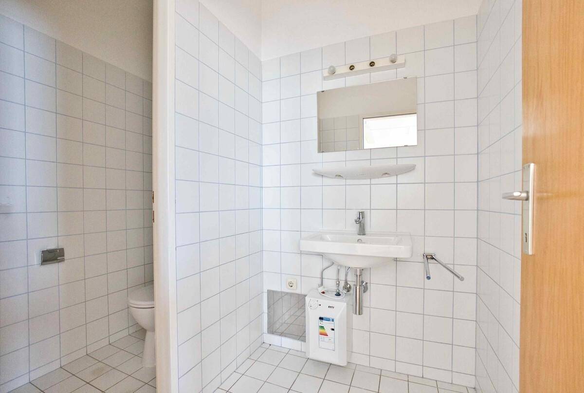 Gefliestes Badezimmer mit Waschbecken, Spiegel und Toilette, ausgestattet mit einem Durchlauferhitzer.