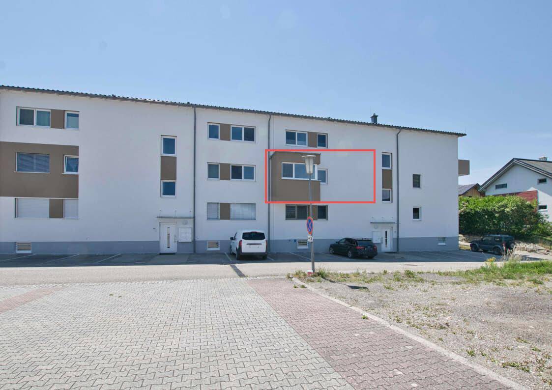 Rückseite eines Mehrfamilienhauses mit Parkplätzen und mehreren Fenstern.