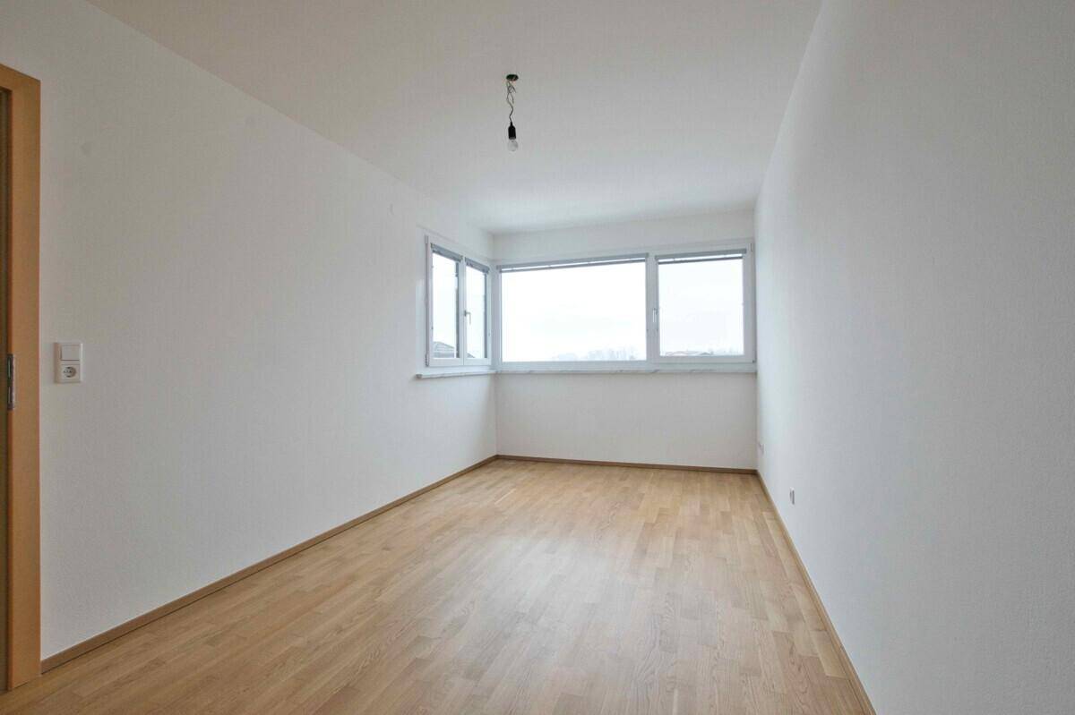 Unmöblierter Raum mit Holzboden und großen Fenstern, ideal für ein Schlafzimmer.