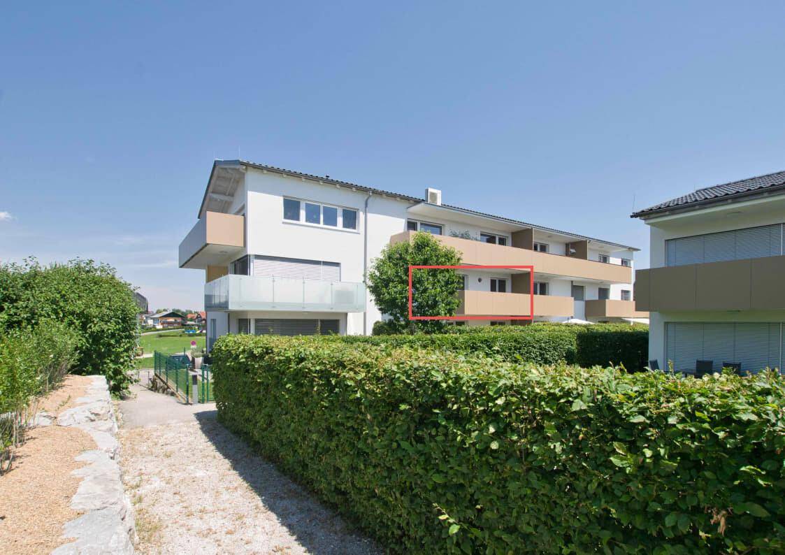 Modernes Mehrfamilienhaus mit Balkonen und grüner Hecke unter klarem Himmel.