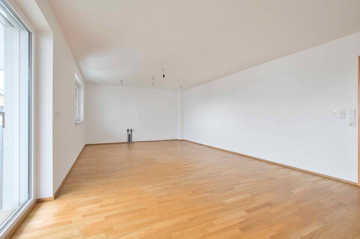 Geräumiger, unmöblierter Raum mit Holzboden und großen Fenstern.