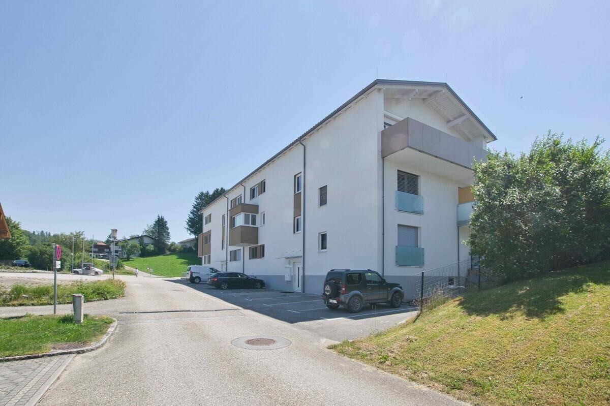 Modernes Mehrfamilienhaus mit Parkplätzen und gepflegter Grünfläche an einem Hang.