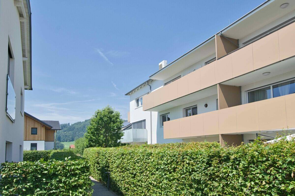 Ansicht eines modernen Mehrfamilienhauses mit mehreren Balkonen und grünen Hecken.