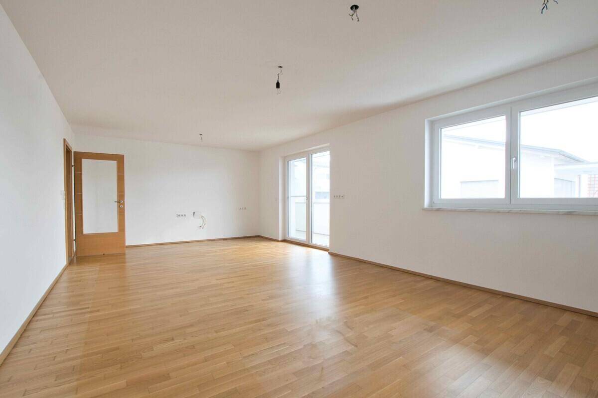 Heller, leerer Raum mit Parkettboden und Zugang zu einem Balkon.