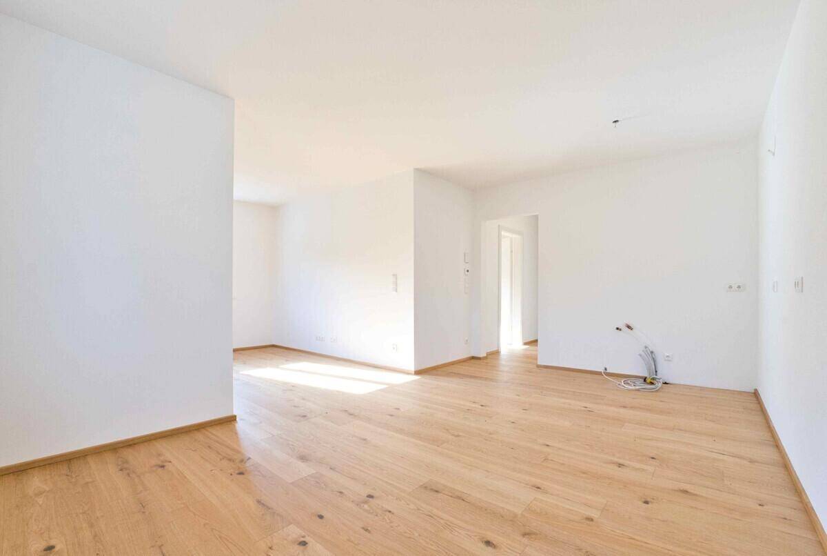 Heller, unmöblierter Raum mit Holzboden und Zugang zu weiteren Zimmern, viel Tageslicht.